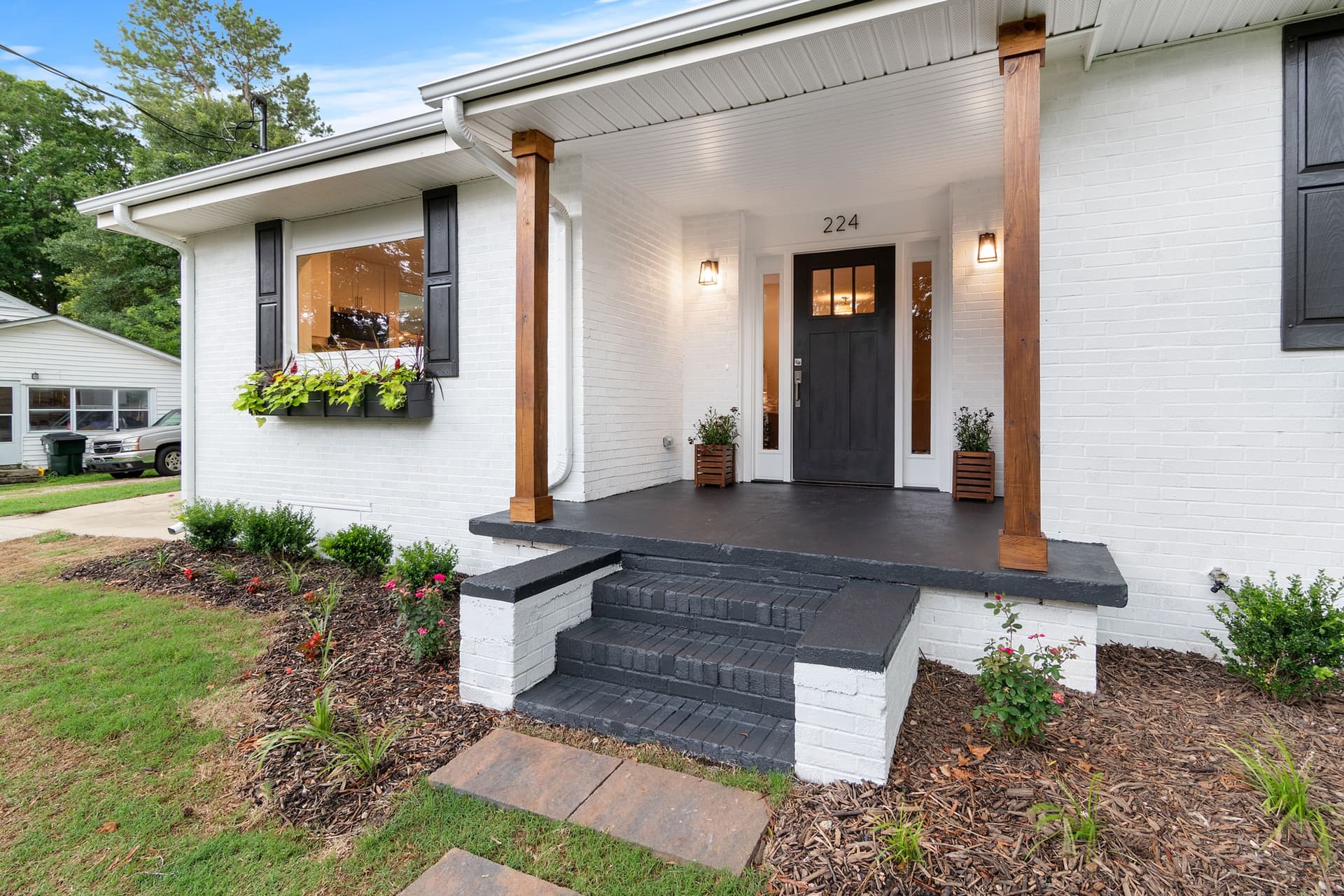 A white-brick home with timber porch columns and a warmly lit entry