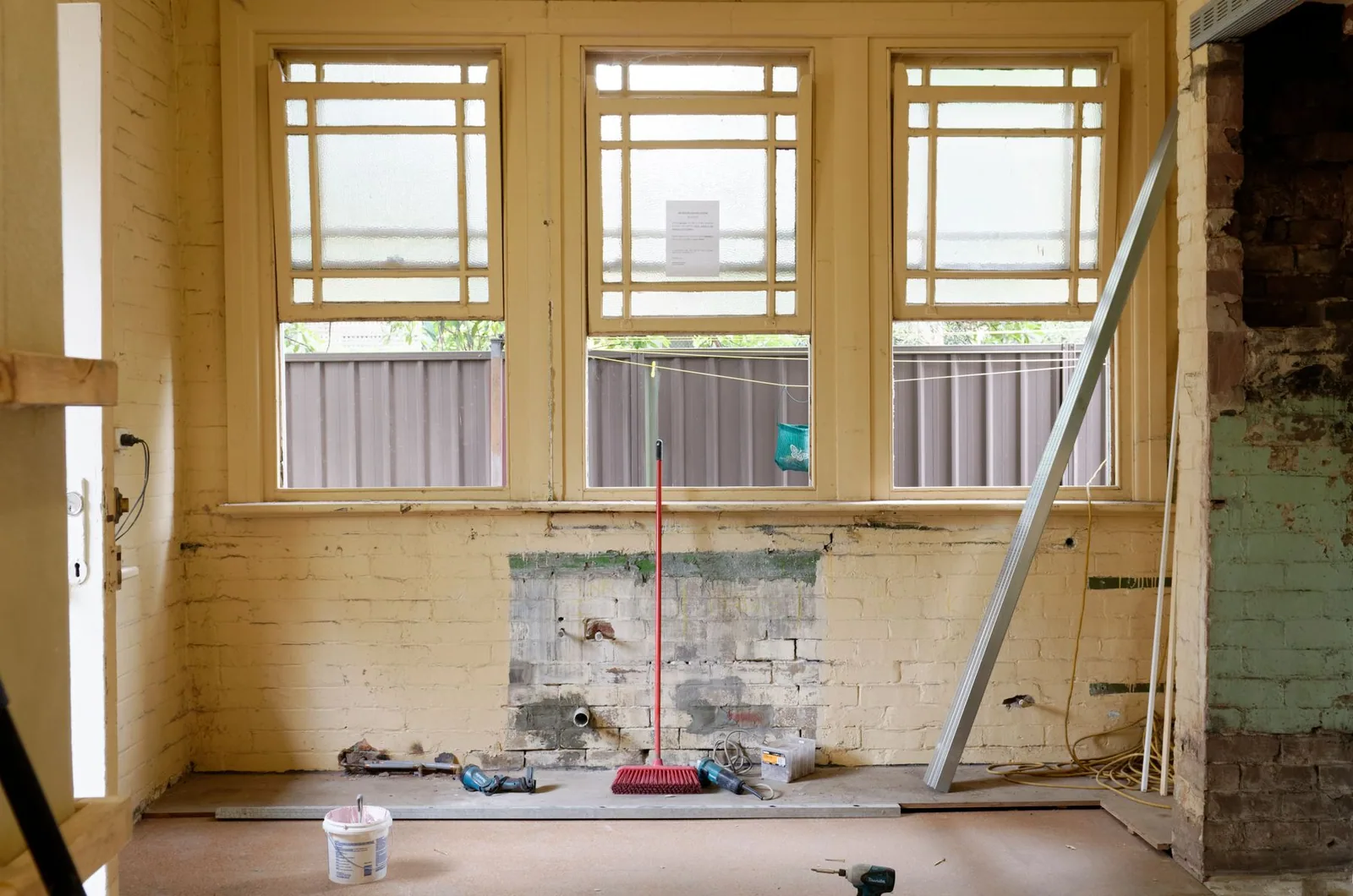 An unfinished room with exposed walls, windows, and renovation tools